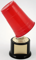 A novelty trophy shaped like an upside-down red plastic cup mounted on a black and gold base with a blank gold plaque, photographed on a white background.