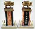 Pig Flaming Column Trophy with a pig resin figure on trapezoid wood base with gold engraving plate, all atop a white marble base that has two golden eagle figures each and gold engraving plates